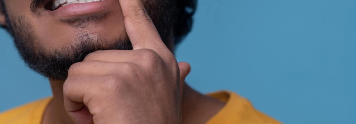A person in a yellow shirt lifts their upper lip with a finger to show their teeth and gums against a blue background.