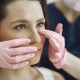 A person wearing pink gloves examines a womans face, gently touching the area under her eyes.